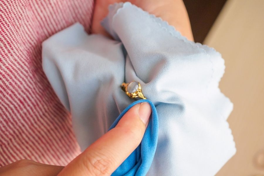A jeweler hand polishing a gold ring with a blue cloth