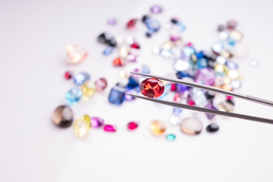 rarest diamond colors - red diamond in tweezers with other colored diamonds on the table 