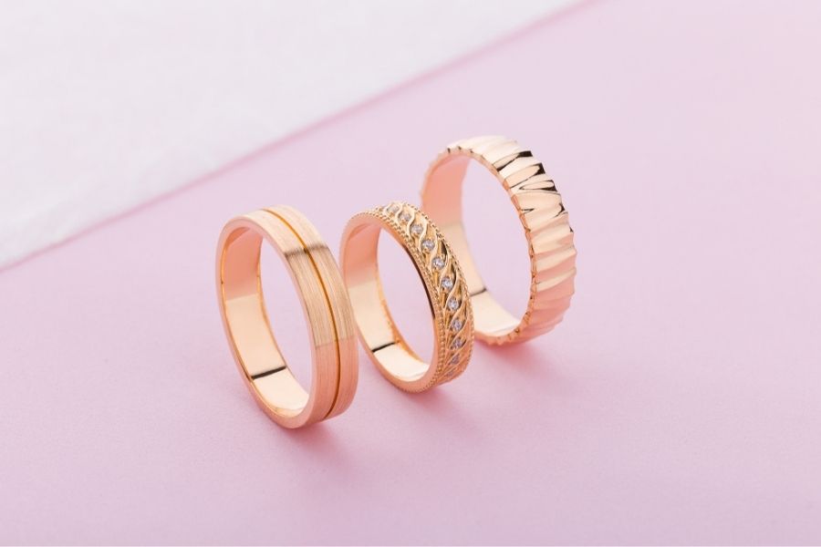 three rose gold rings on pink surface