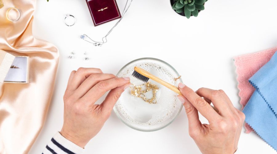 top view of the hands of a woman cleaning a gold chain using a micro bristle toothbrush