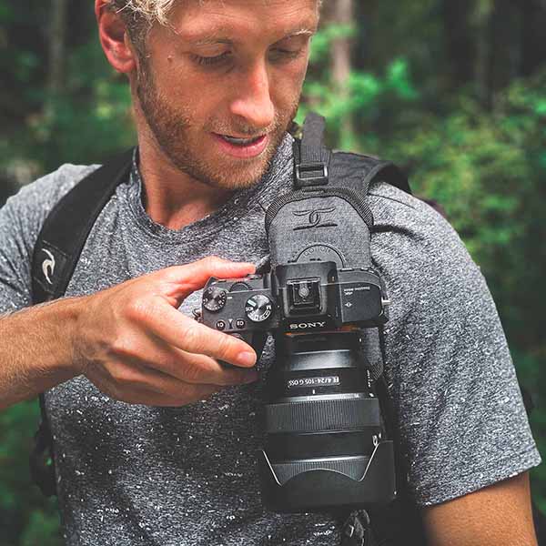 Man wearing a CCS G3 Strapshot camera harness and looking at his camera while hiking