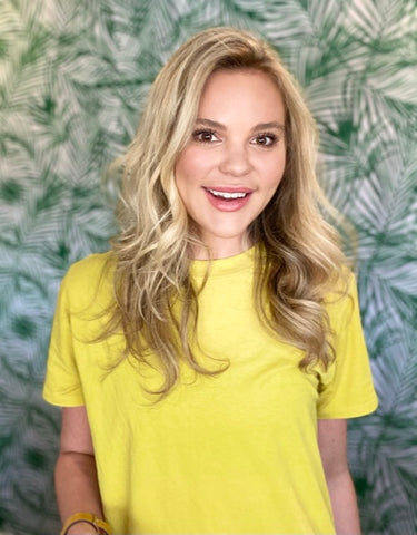 Courtney Broder, a blonde caucasian woman wearing a yellow shirt in front of a palm tree print background