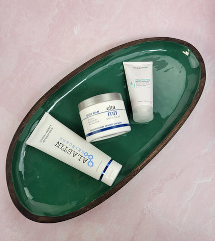 Alastin Soothe and Protect Balm, EltaMD Laser Balm, and ClarityRX Healing Fine Balm laying on a green platter
