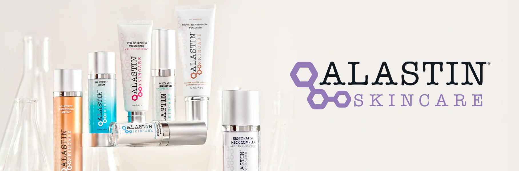 Several Alastin Skincare products standing with glass beakers against a beige background with the Alastin Skincare logo