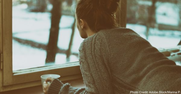 Sad woman by the window with y cup of coffee in a hand