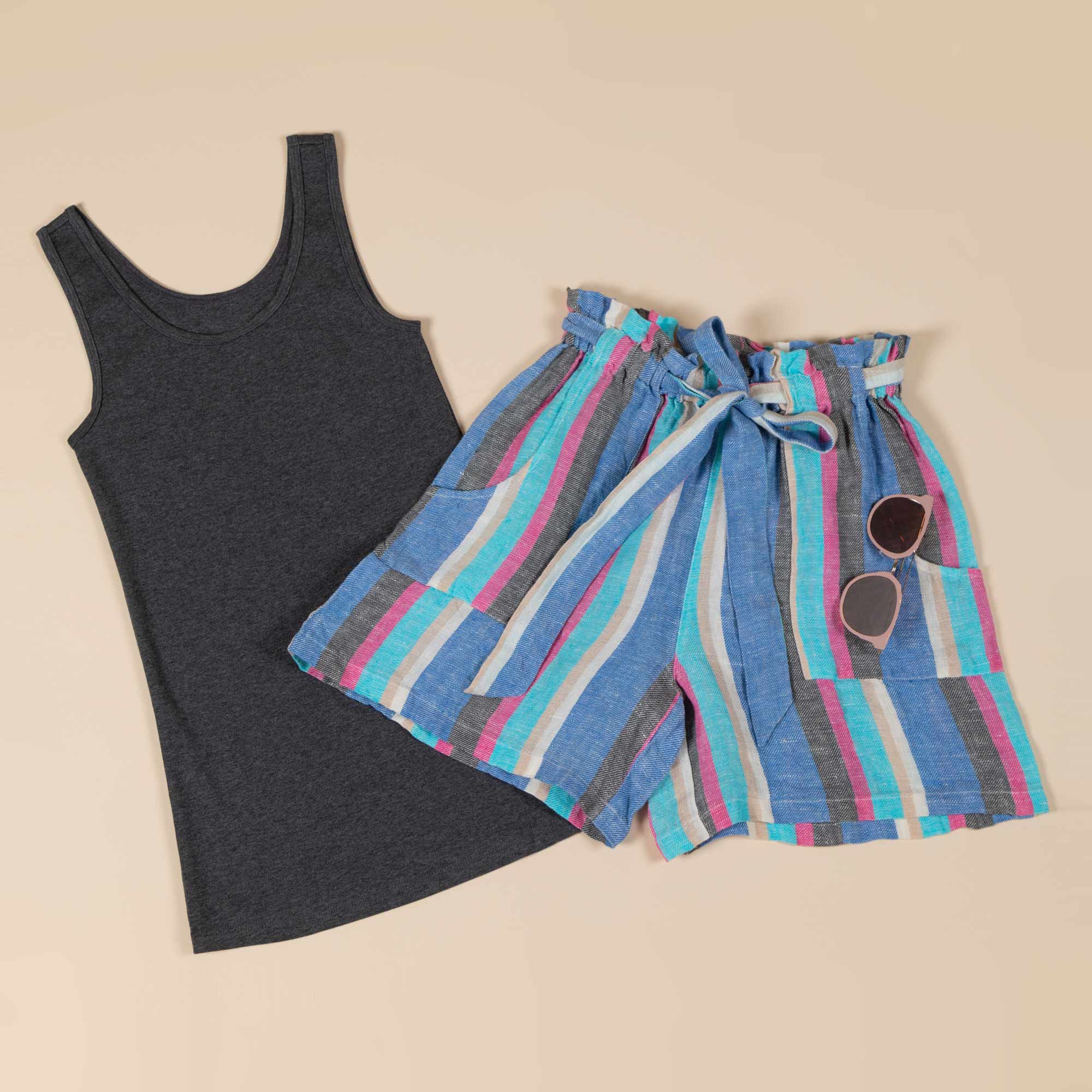 Artisan crafted shorts — with sunglasses hung on the pocket — lay atop a solid colored tank top.