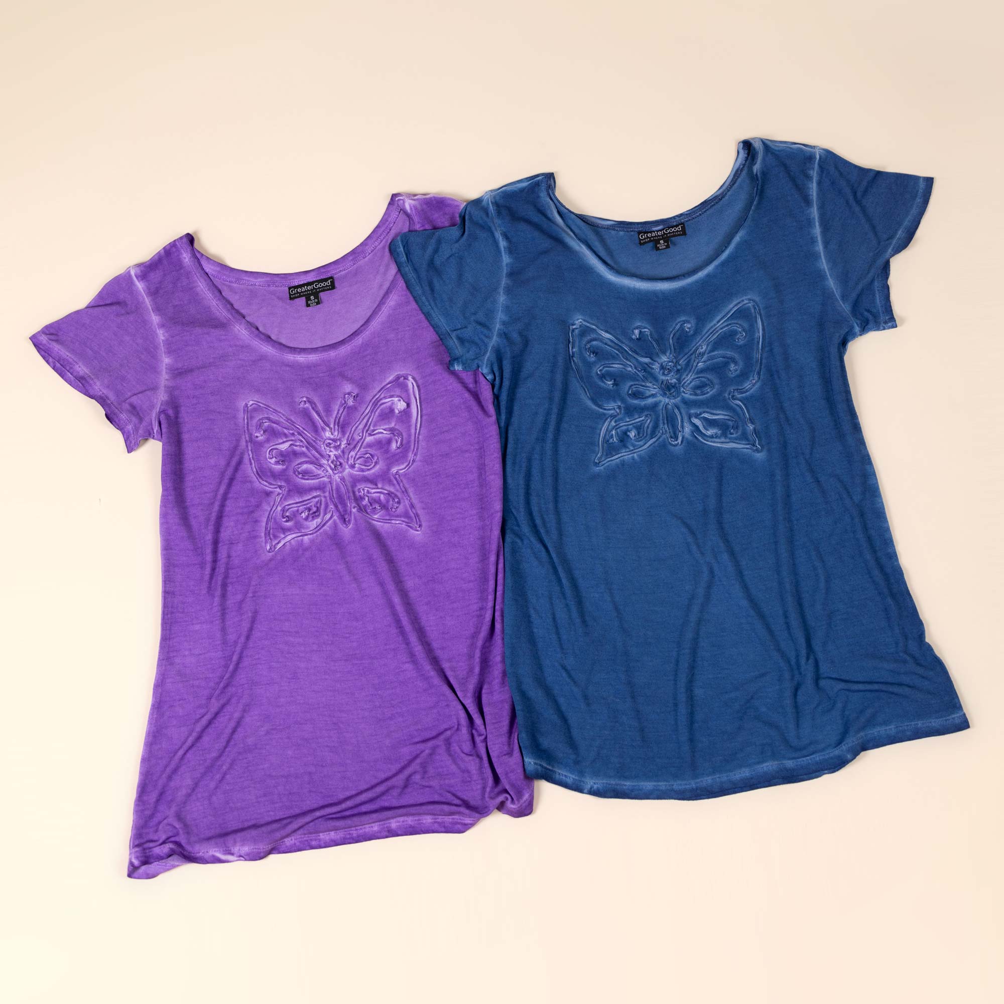 A purple, and a blue t-shirt — each with a handwoven butterfly design