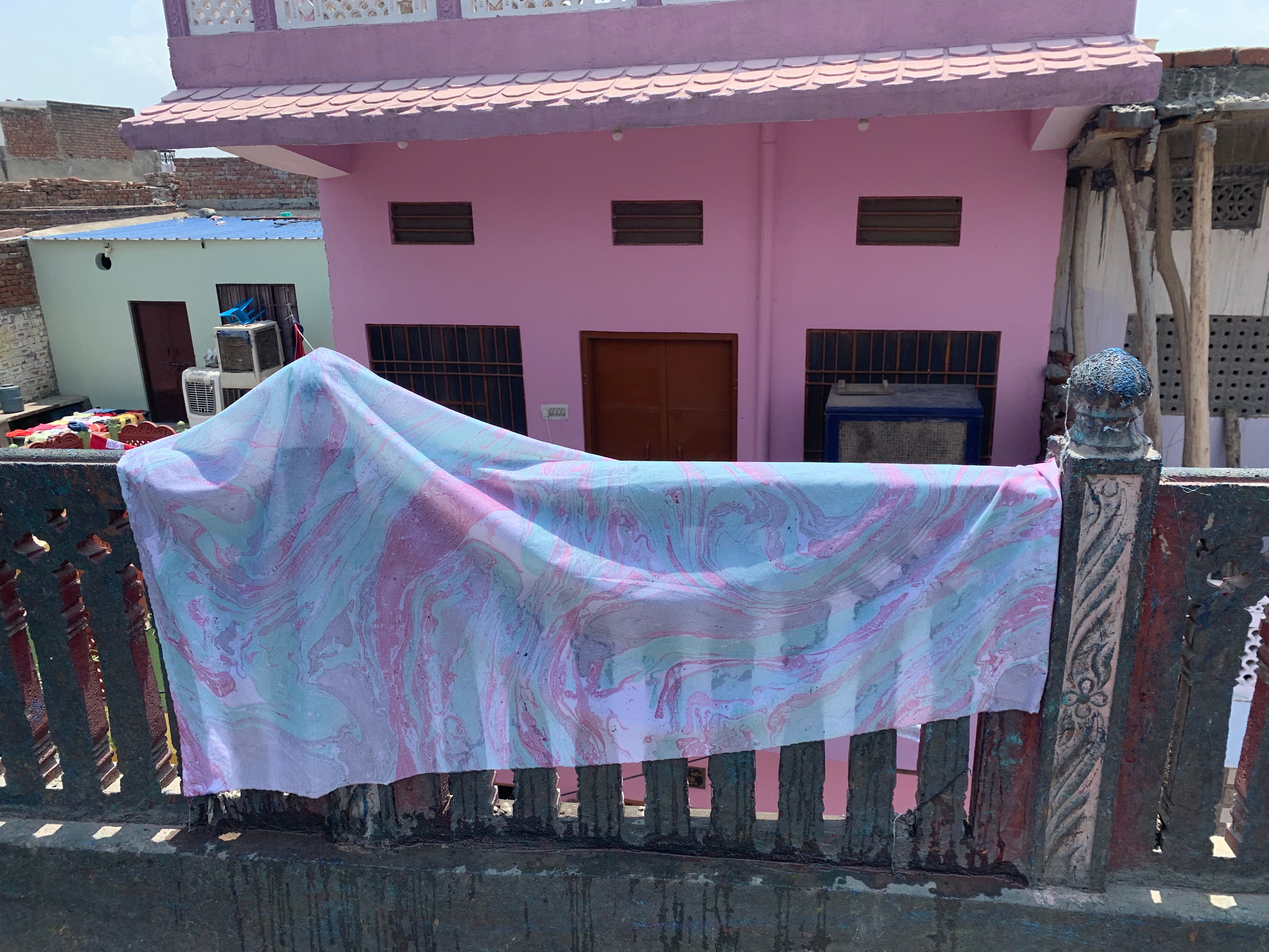 Fabric, infused with a tie-dye patten, dries outside on a stone fence next to an artisan facility