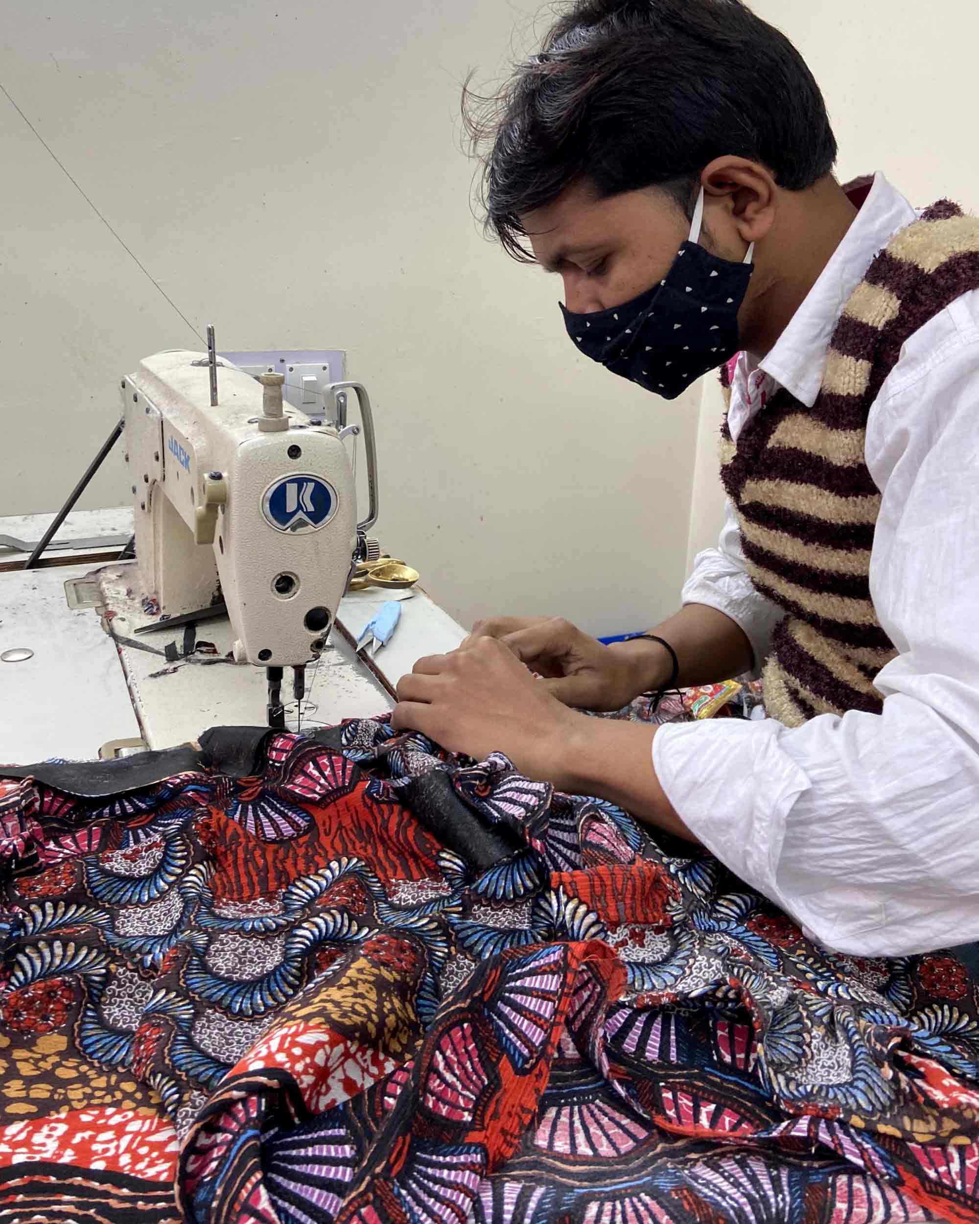 An artisan carefully sowing a dress using whimsical fabric