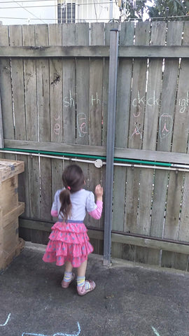 little girl jumping to slap phonograms on fence