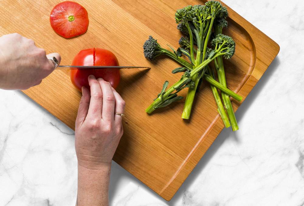 Best cutting board: A hand slices tomatoes on the Misen Trenched Cutting Board