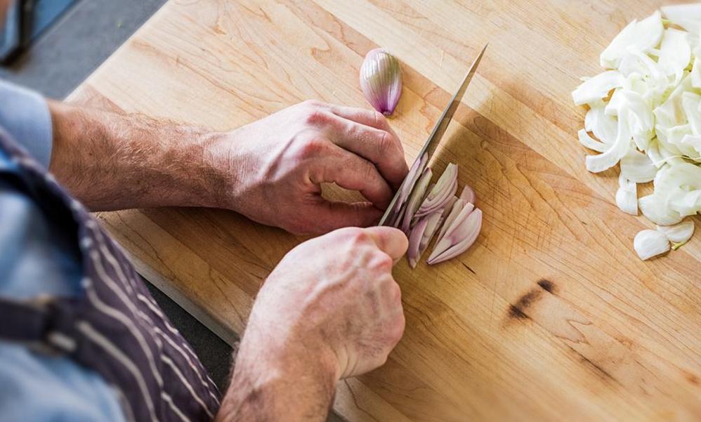 A home cook slices shallots with a santoku knife, one of the more useful types of kitchen knives