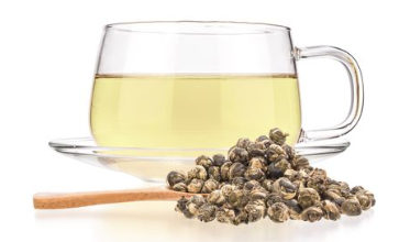 Glass cup and saucer of jasmine tea pearls with a small pile of Jasmine Tea pearls in the foreground.