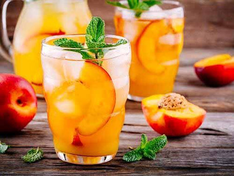 Peach Tea Punch in a short glass on a wood table with half a peach next to the glass