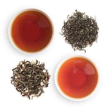 Two white tea cups filled with Breakfast Blend Tea and a small pile of the tea leaves next to each tea cup.