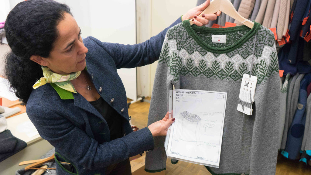 woman holding up a paper with the design of a sweater in front of the actual wool sweater