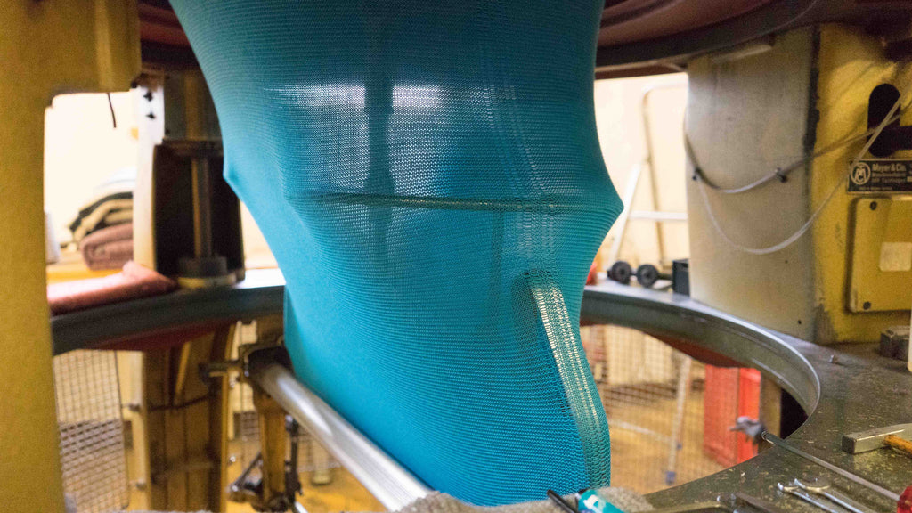 knitted blue wool fabric coming out of the bottom of a left left knitting machine