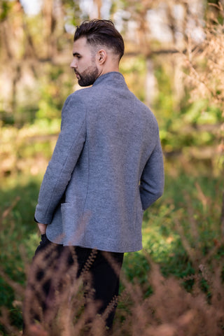 young man wearing traditional Austrian boiled wool jacket in gray standing in meadow 