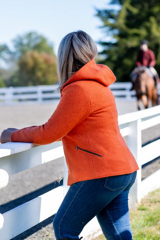 woman watching horseback rider while wearing orange boiled wool hoodie from Robert W. Stolz