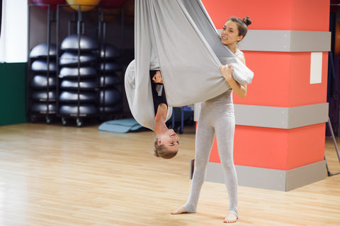2 girls helping each other out while  practicing aerial yoga