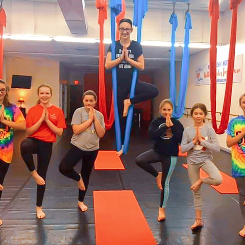 A group of girls doing a tree pose in an aerial yoga studio