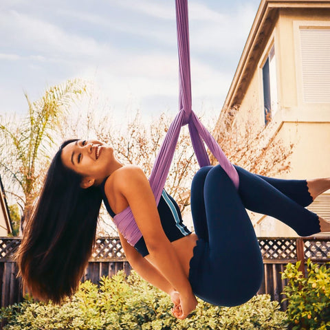 Smiling girl hanging on a purple aerial hammock in her backyard