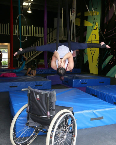 Upside-down split in a black aerial hammock in front of a wheelchair