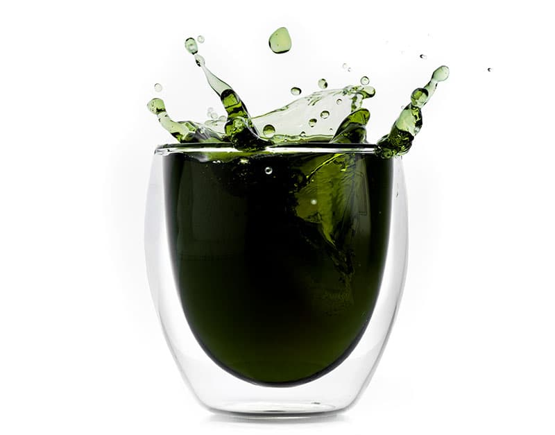 glass of liquid chlorophyll splashing as ice cubes land in it