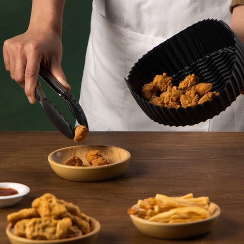 person taking nuggets from the Uber Appliance Air Fryer Reusable Silicone liner with tongs and placing them into a dish in a kitchen setting