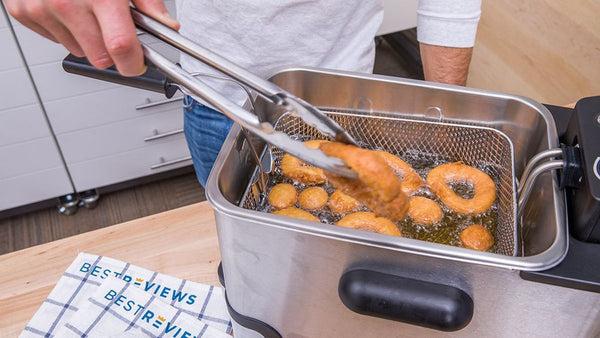 Person Frying onion rings in an brushed stainless steel deep fryer with black handles and a stainless steel mesh basket