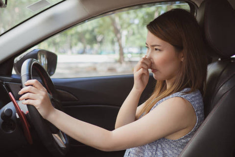 Woman driver blocking her nose to avoid smelling bad odor in the car