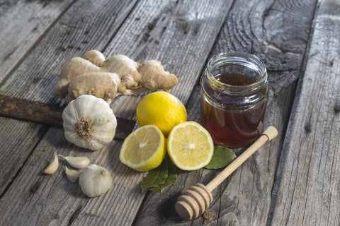 A jar of honey sits on a wooden table with lemons, garlic, and ginger 