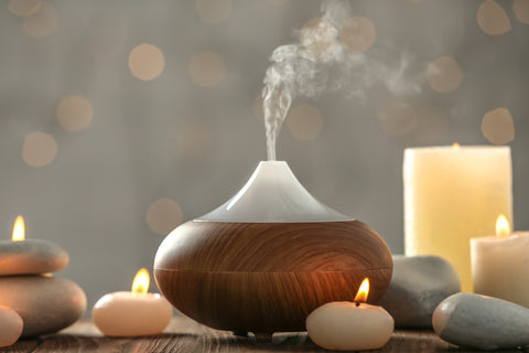 An essential oil diffuser emits steam surrounding by lit tea candles