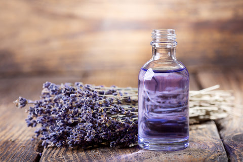 A glass bottle sits on a wooden table with a lavender plant
