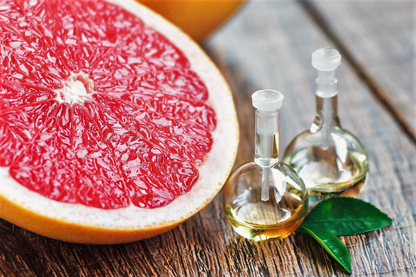 Two small bottles with oil sit on a wooden table besides a piece of grapefruit