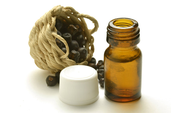 A mini woven basket filled with Juniper berries sits behind an amber-colored bottle and a white cap 