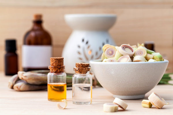 Two mini glass bottles with cork tops sit side by side in the foreground - one with clear oil, one with yellow - on a table next to a white bowl 