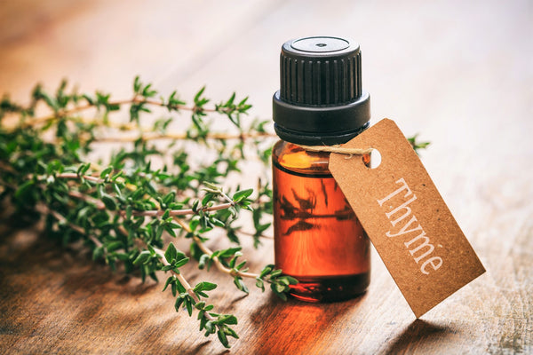 An amber-colored bottle with a carboard tag that says 'Thyme' sits on a wooden table next to Thyme leaves