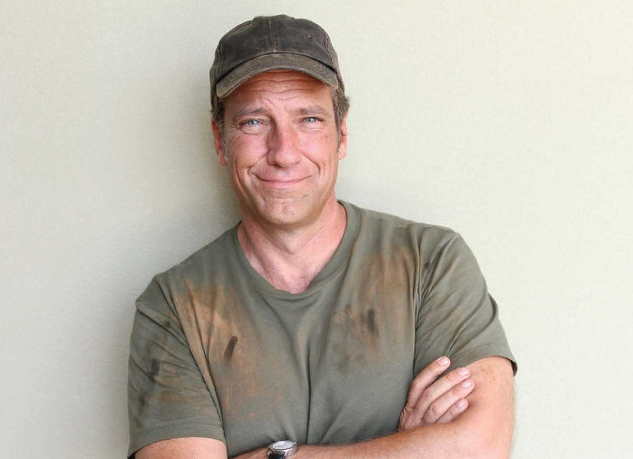 Man with a dirty shirt and cap, arms crossed, smiling at the camera.