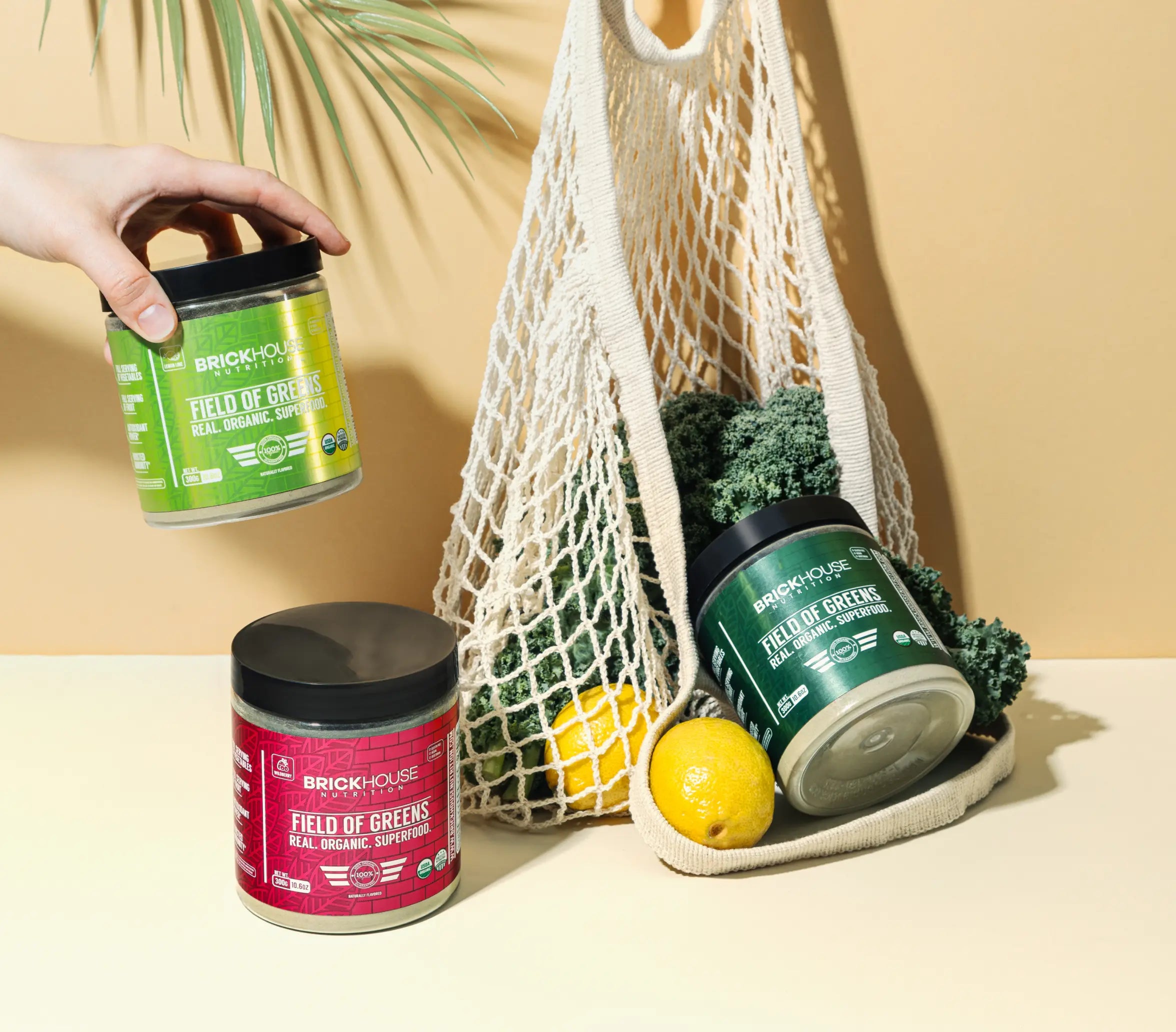 Three containers of BrickHouse Nutrition's 'Field of Greens' superfood with a produce bag containing kale and lemons.