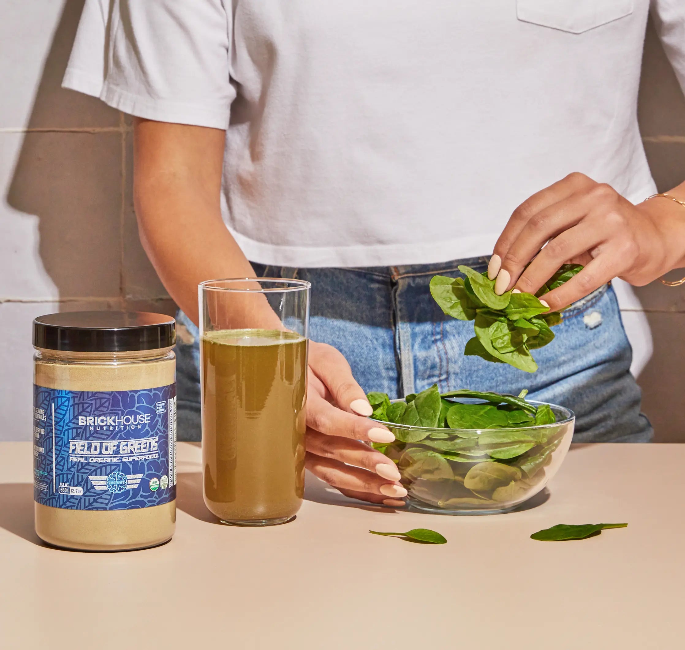 Person preparing greens with a supplement jar and green beverage on the table.