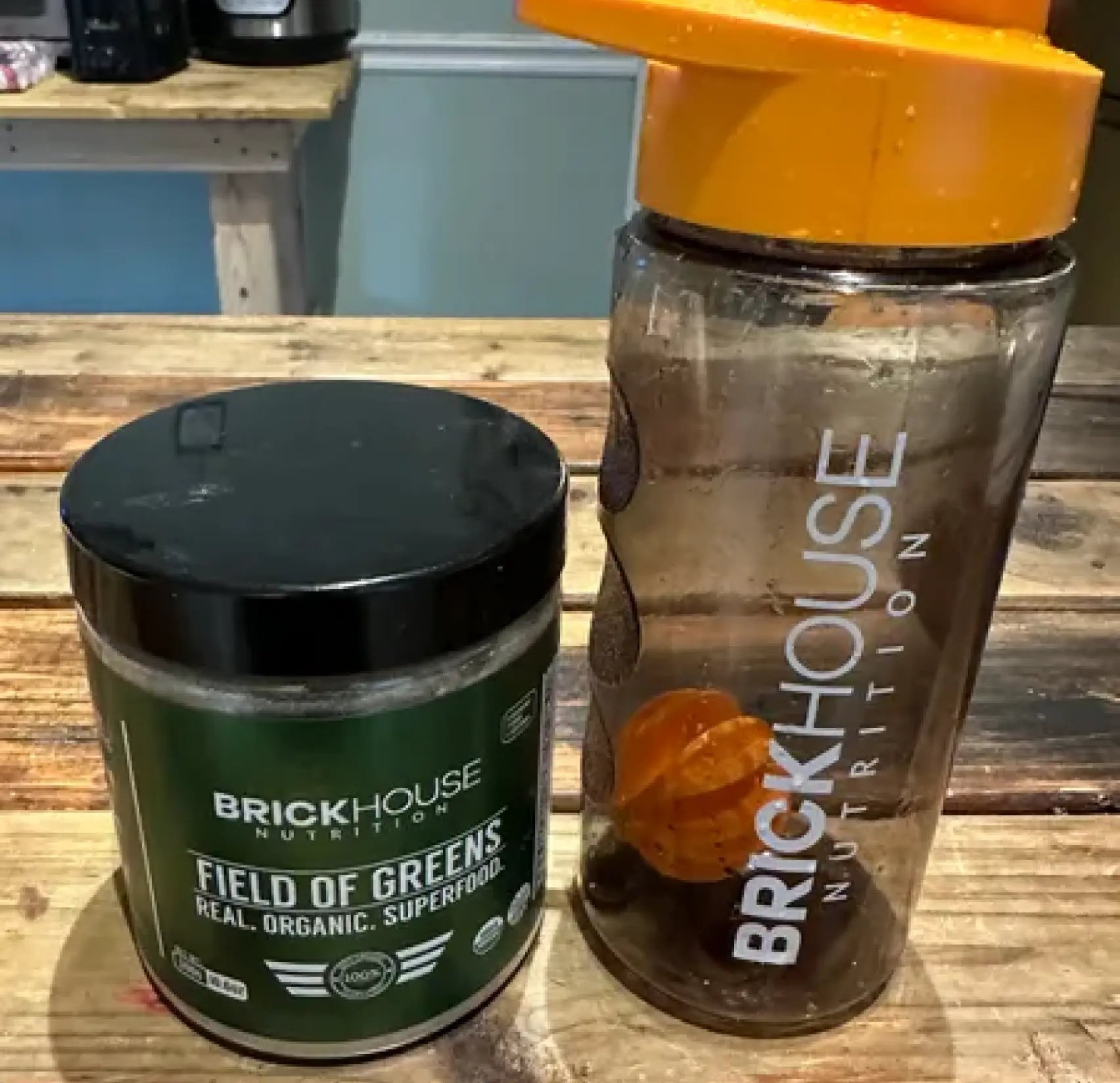Container of BrickHouse Nutrition's superfood powder next to a BrickHouse shaker bottle on a wooden table.