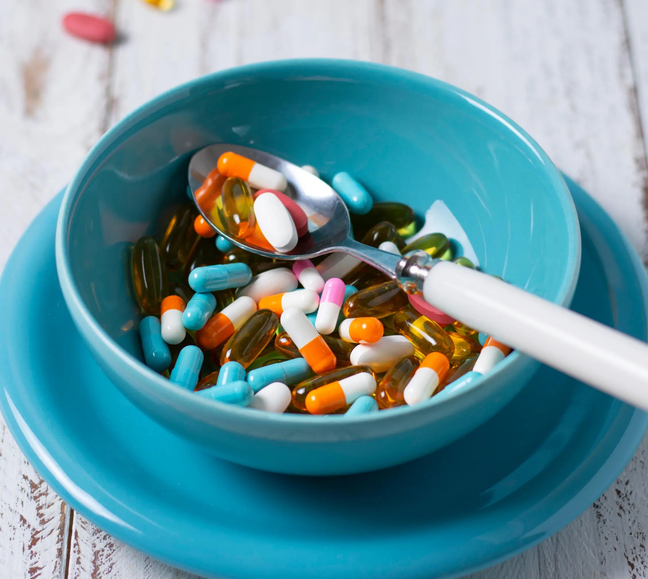 A bowl and spoon filled with various colorful pills and capsules.