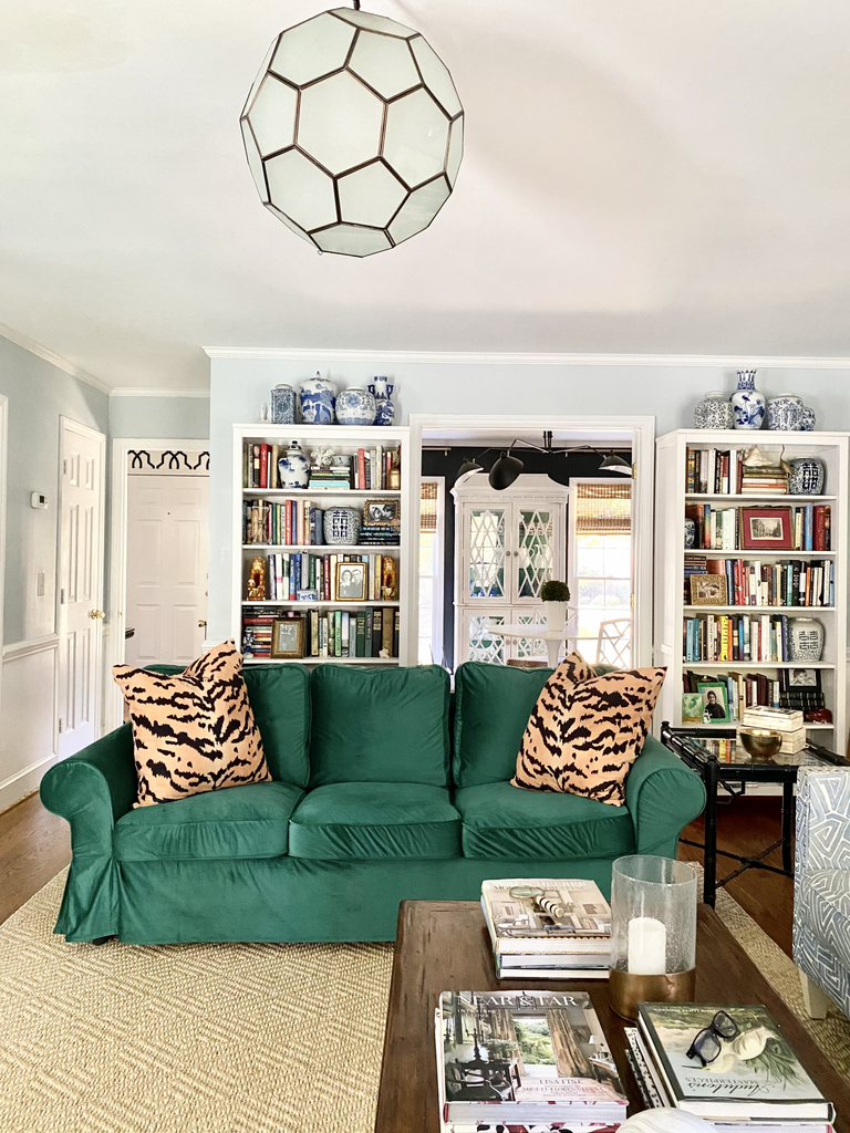 A lively lounge space with a green sofa, decorative cushions, and shelves stacked with books and ornaments.