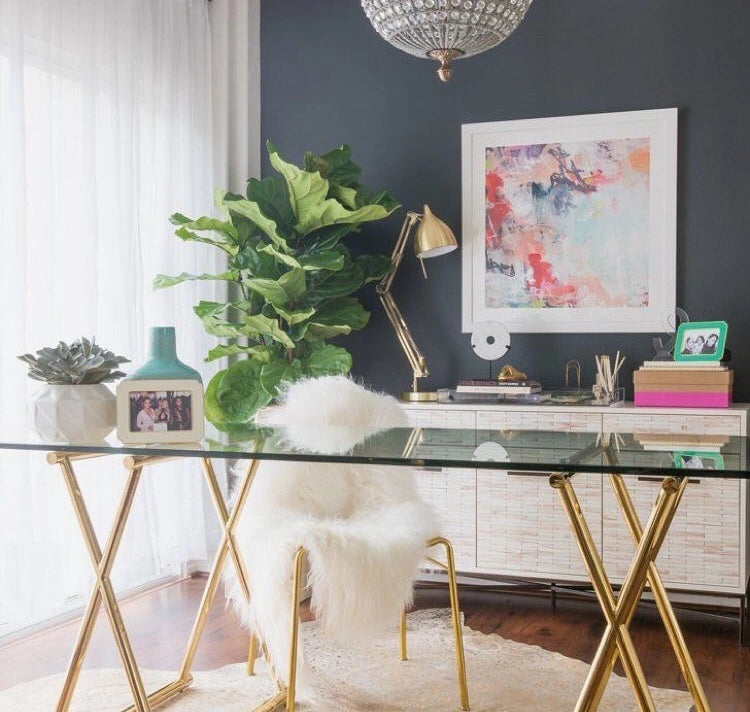 A transitional, naturally-lit room with wall art and a central glass table.