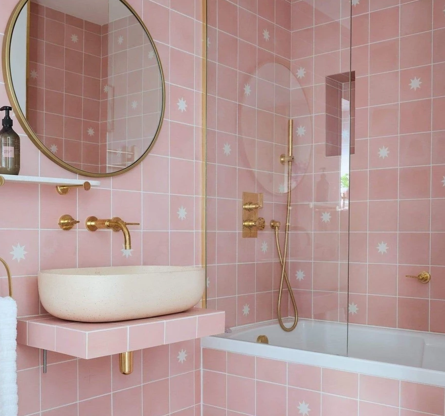 A pink-tiled bathroom with shower bath, sink, and mirror
