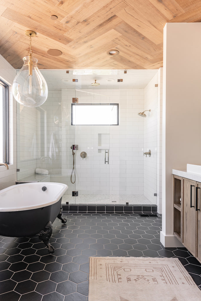 a modern bathroom with black floor tiles, pale hexagonal wall tiles, and a wooden sink unit.