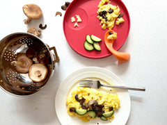 two plates with scrambled eggs, sautéed mushrooms, and cucumbers