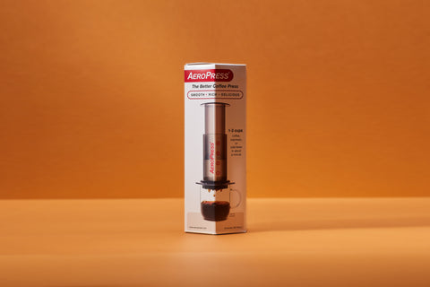 A boxed Aeropress photographed on an orange background.