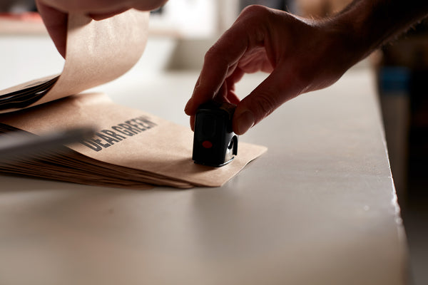 A Dear Green Coffee Roasters staff member stamps our logo on to our brown craft paper bag.